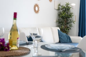 Un soggiorno moderno con un divano bianco, un tavolo da pranzo con piatti e bicchieri, una bottiglia di vino e una pianta in vaso.