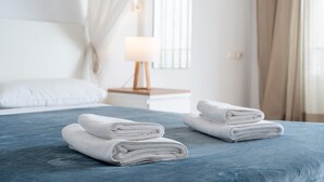A neatly made bed with folded white towels, a bedside lamp, and a window with curtains.