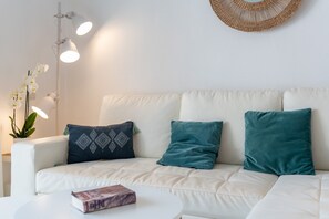 A white sofa with teal cushions, a white side table with a book, and a wall-mounted light fixture. - Beach Front house - Full Sea view - Dona Lola Beach Resort - Marbella - Mijas (Marbella)