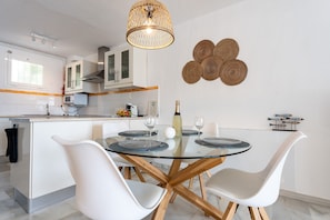 Une cuisine moderne avec des meubles blancs, une table à manger en verre et une décoration murale originale faite de fibres tressées.