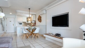Ein modernes Wohnzimmer mit Essbereich, einem an der Wand montierten Fernseher und einer Küche im Hintergrund.