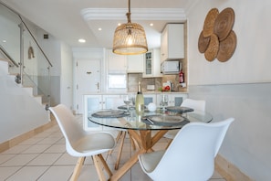 A modern kitchen with a glass dining table, white chairs, and a hanging light fixture.