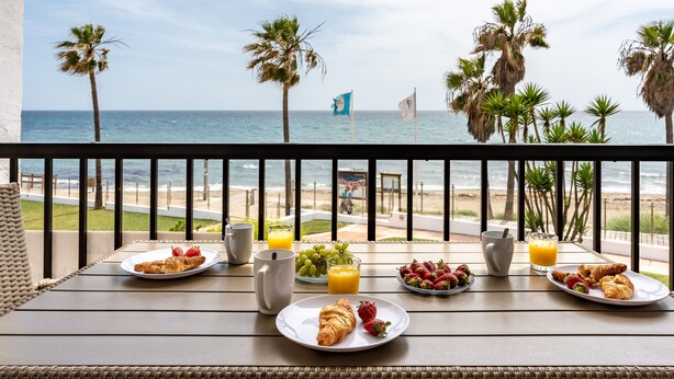 Ein Balkon mit Frühstücksangeboten, Blick auf den Strand und Palmen.