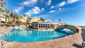 Ein Pool mit gefliestem Sonnendeck, Palmen und einem Gebäude mit großen Fenstern.