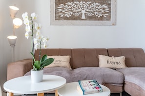 A living room with a sofa, a round white table, a potted orchid, a framed tree artwork, and a book.