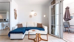 Ein modernes Wohnzimmer mit einer Couch, zwei Beistelltischen, einem Wandkunstwerk und einer Glastür, die zu einem Außenbereich führt.