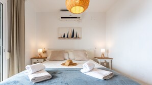 Ein Hotelzimmer mit einem Bett, zwei Nachttischen, einer Wand-Klimaanlage und einem Gemälde über dem Bett.