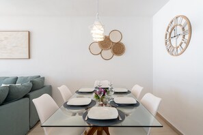 Un espace repas moderne avec une table en verre, des chaises blanches et une horloge murale décorative.