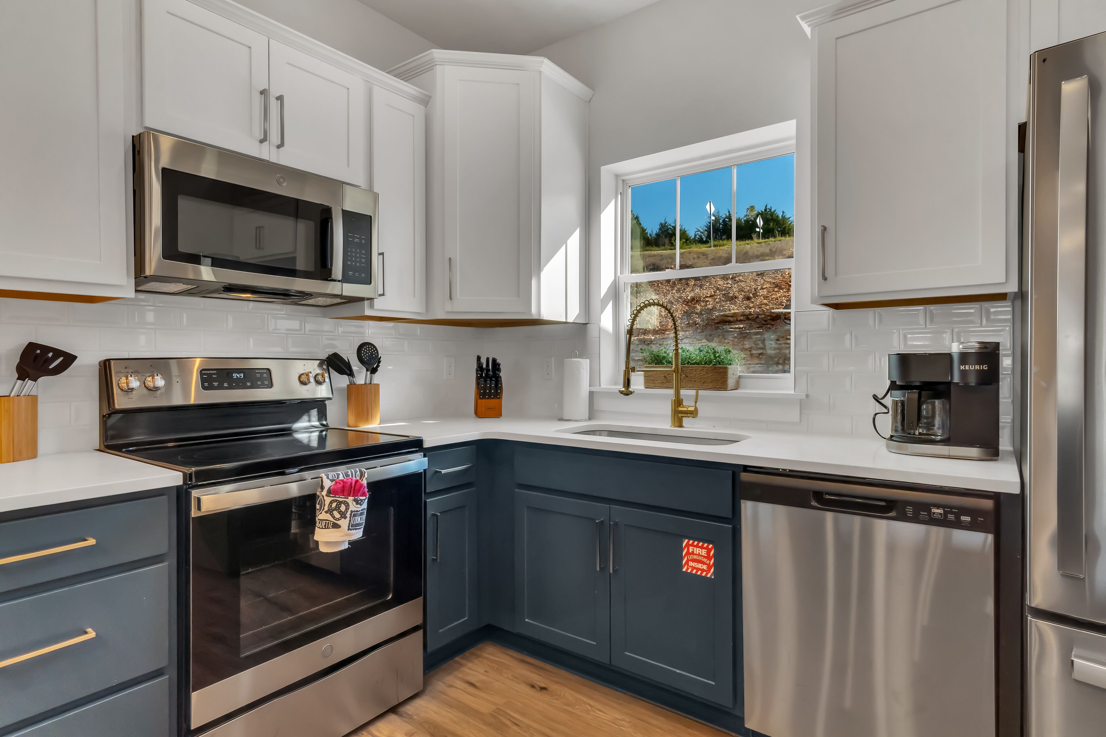 A modern kitchen with stainless steel appliances, white cabinetry, and a window with a view of greenery.