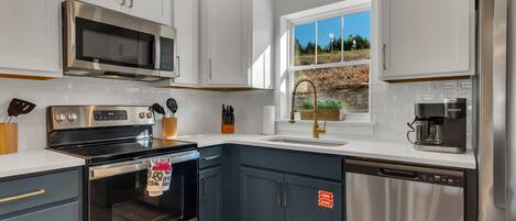 A modern kitchen with stainless steel appliances, white cabinetry, and a window with a view of greenery.