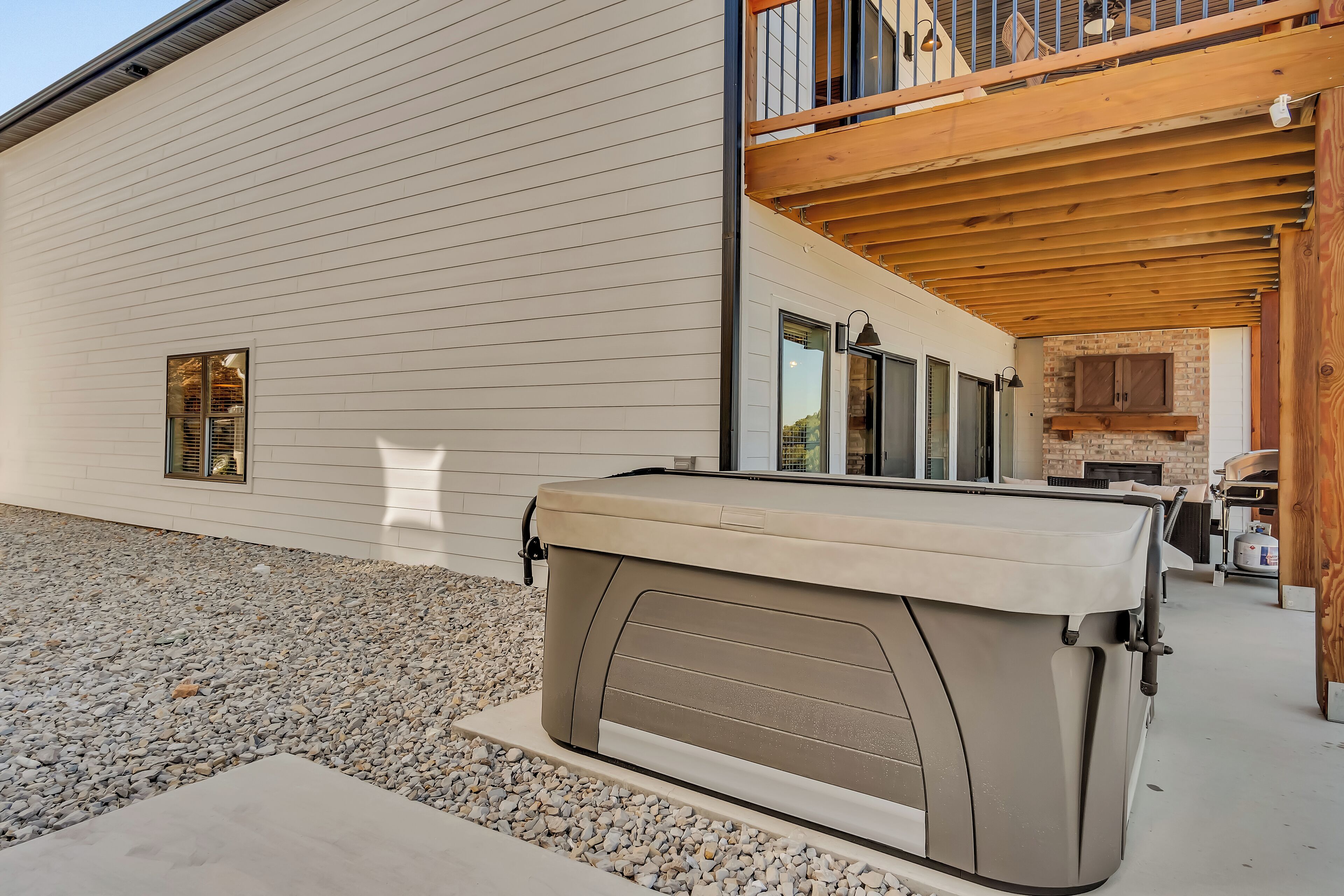 A covered outdoor seating area with a hot tub, a wooden deck, and a brick fireplace.