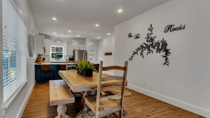 Una cocina moderna con armarios blancos, un refrigerador de acero inoxidable y un comedor con mesa y sillas de madera.