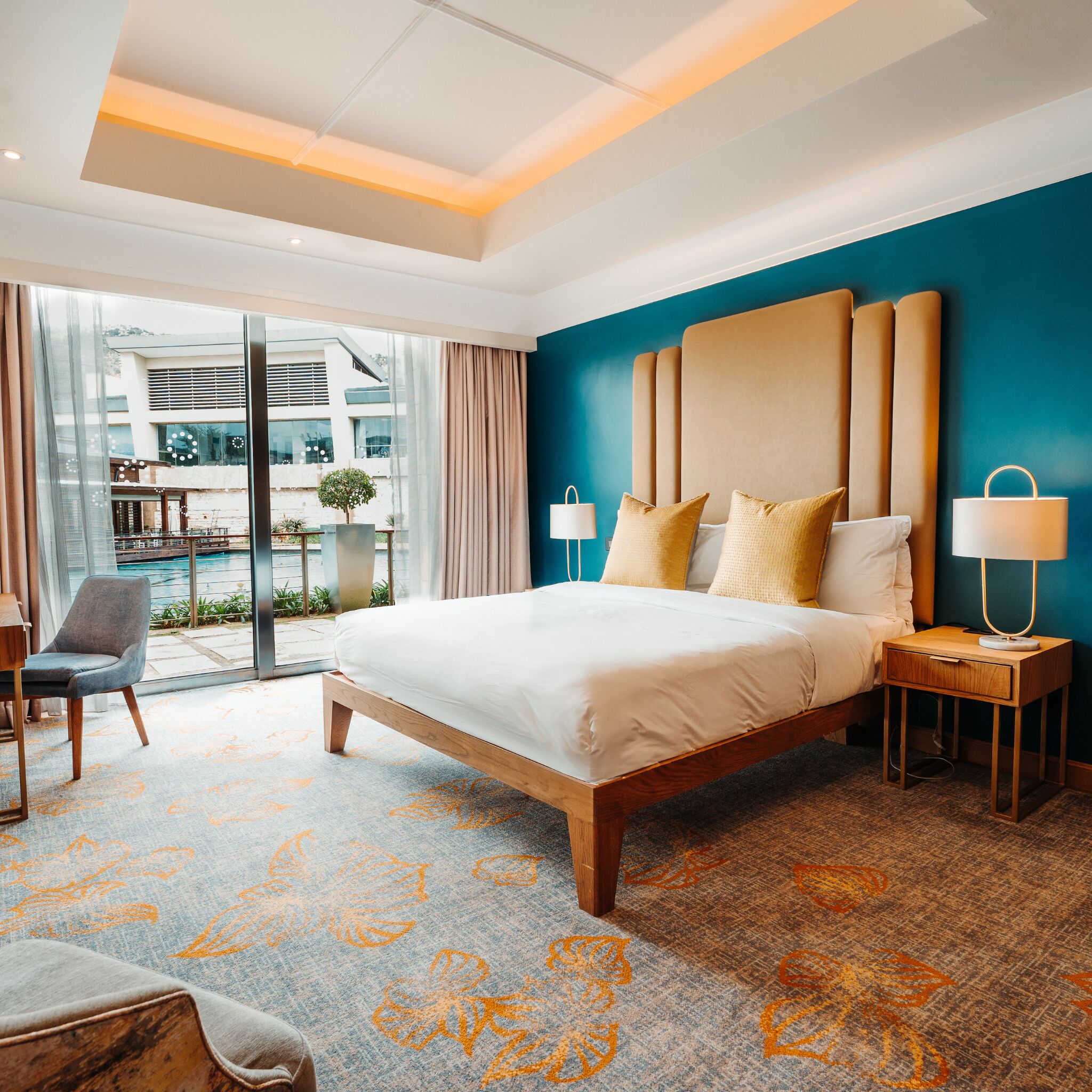 A hotel room with a large bed, a nightstand, a chair, and a view of the outside.