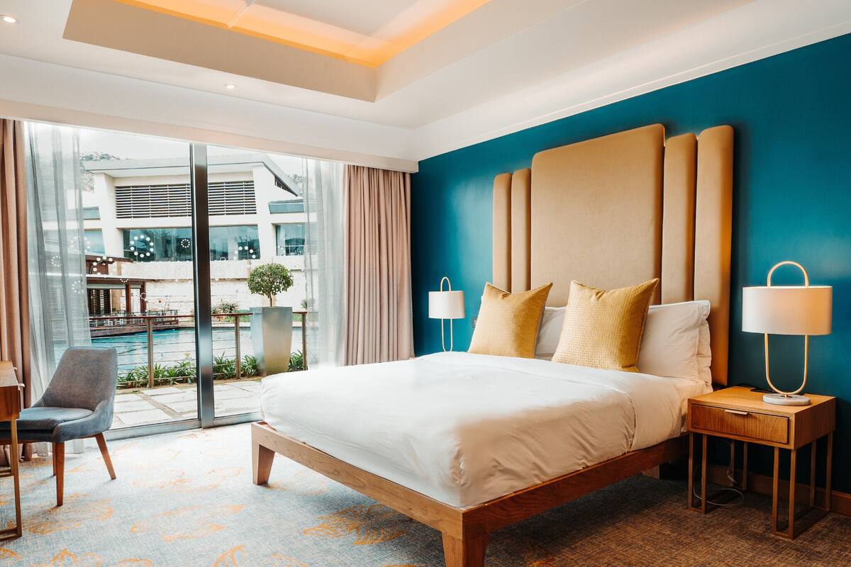 A hotel room with a large bed, a nightstand, a chair, and a view of the outside.