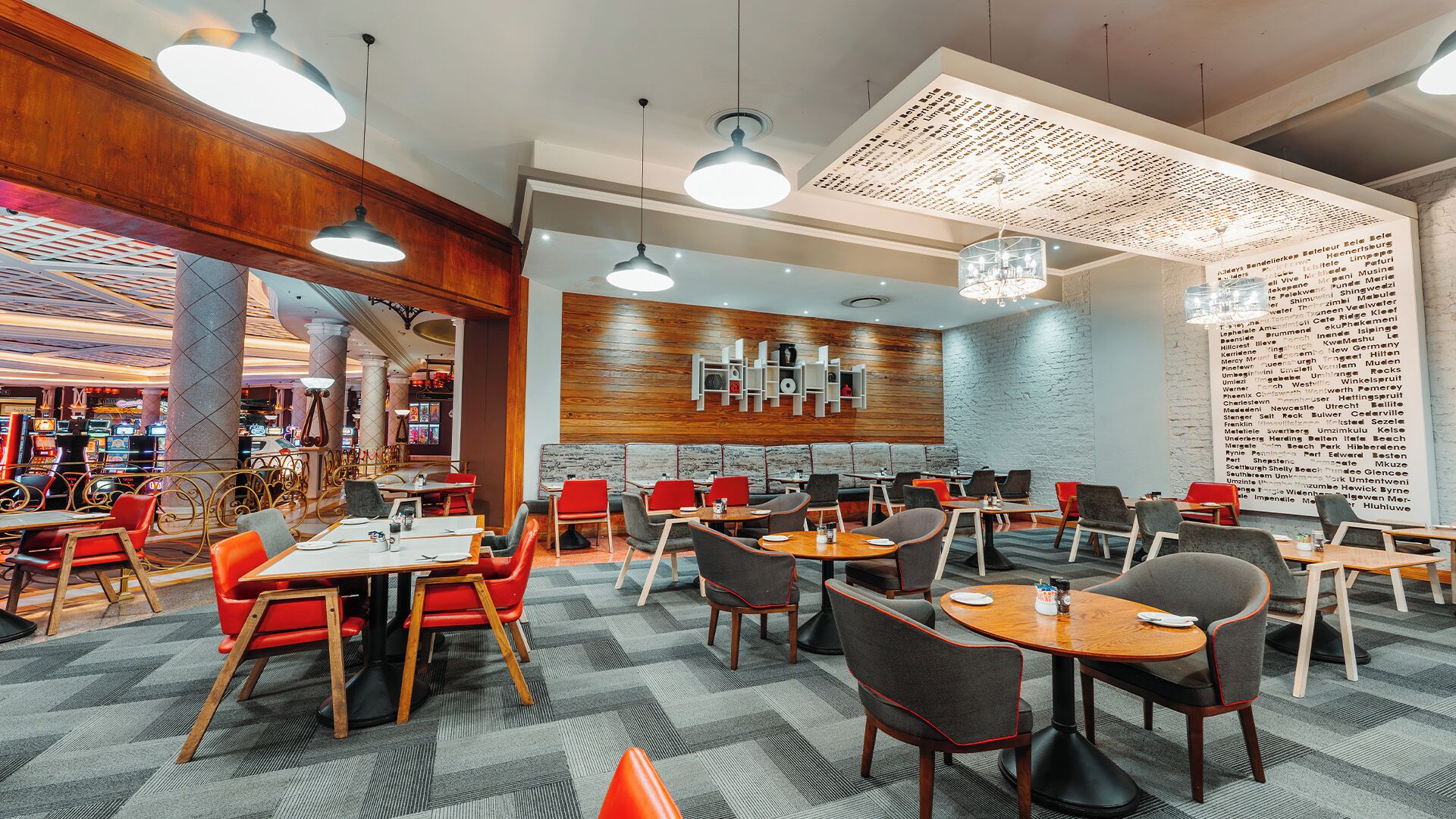 A modern restaurant with a mix of booth and table seating, a patterned carpet, and pendant lighting.