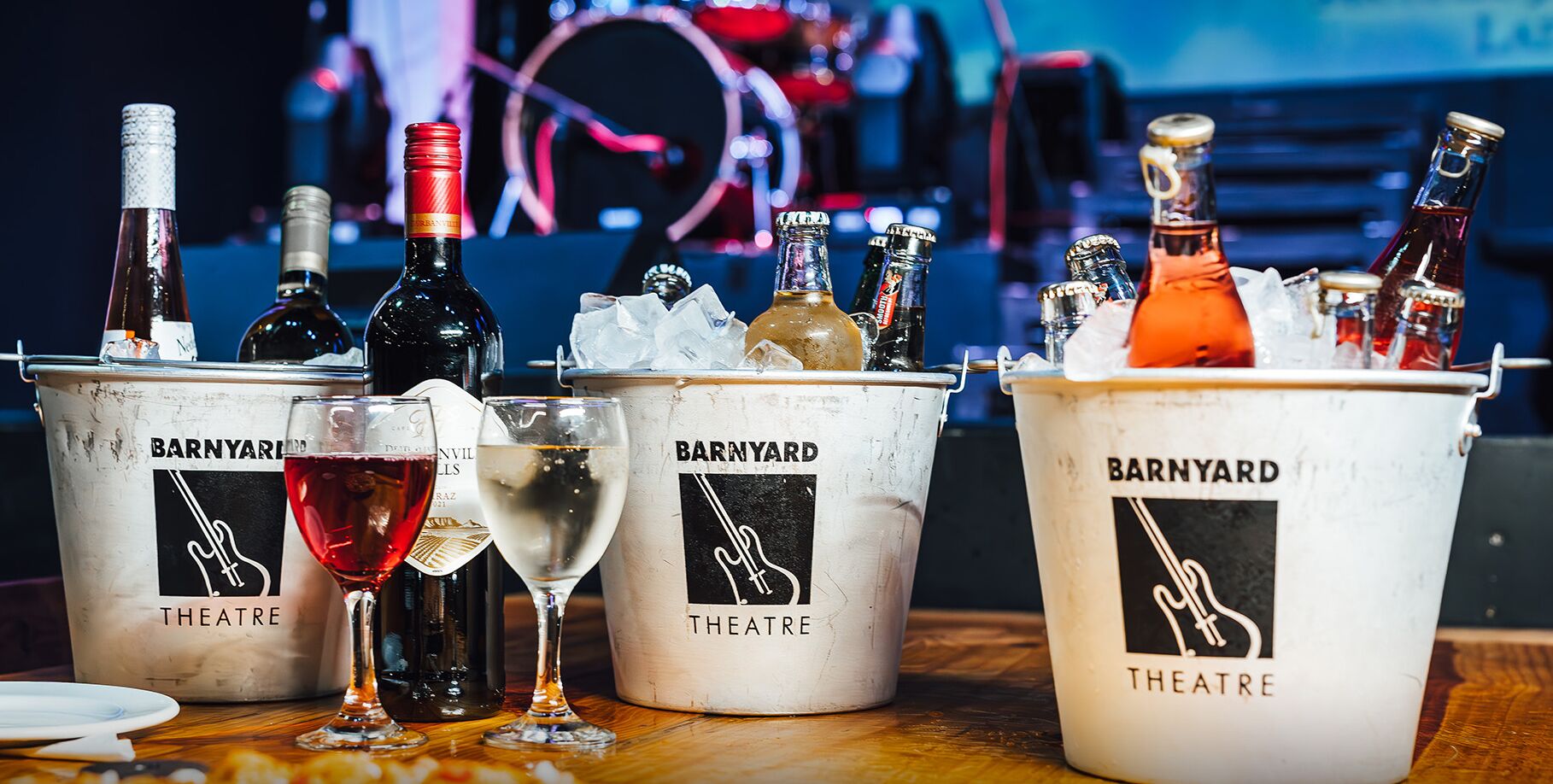 Three buckets labeled "BARNYARD THEATRE" with various bottles and glasses of beverages.