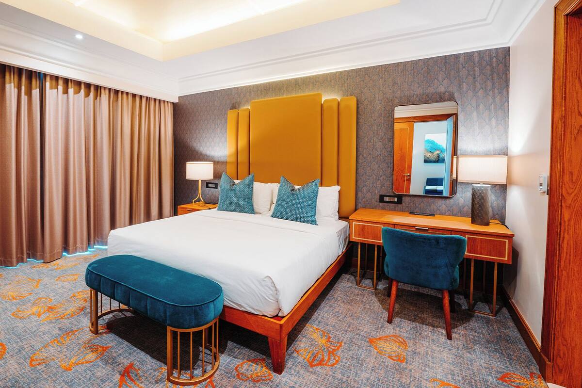 A hotel room with a large bed, a desk, a chair, a mirror, and a window with curtains.