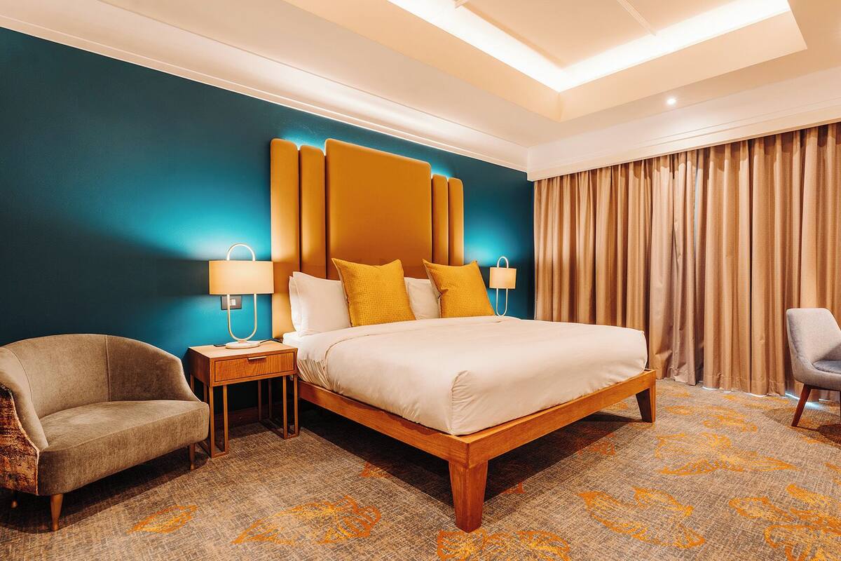 A hotel room with a large bed, a desk, a chair, and a nightstand with lamps.