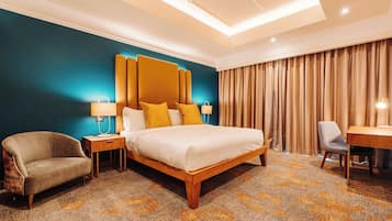 A hotel room with a large bed, a desk, a chair, and a nightstand with lamps.