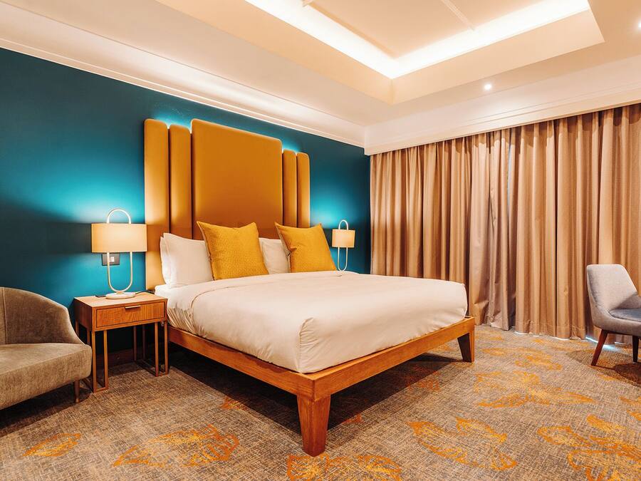 A hotel room with a large bed, a desk, a chair, and a nightstand with lamps.