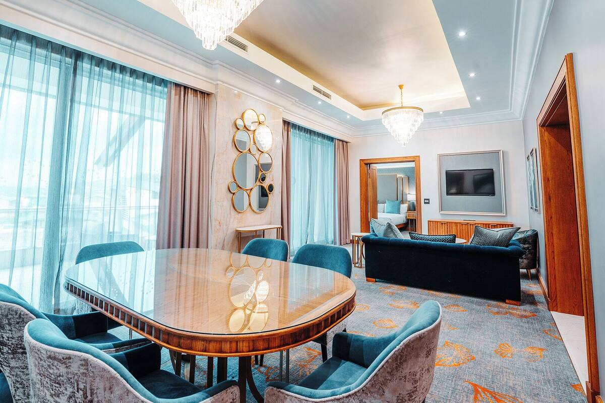A spacious room with a large oval table, comfortable seating, a sofa, a TV, and a chandelier.