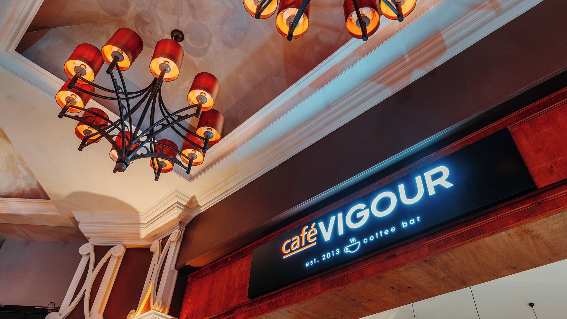 A café interior with a modern chandelier and a neon sign for Café Vigour.