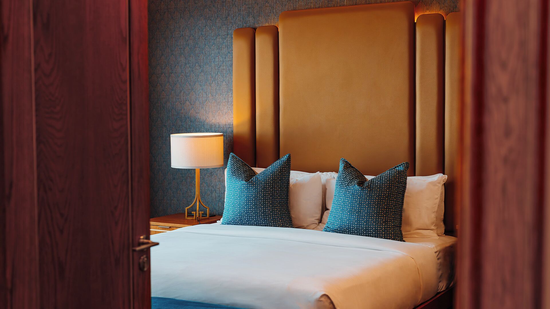 Habitación de hotel con una cama grande, cabecera de madera y pared con diseño.