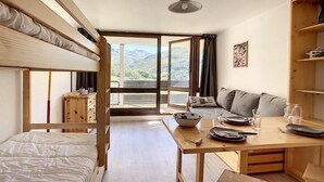 Una stanza con un letto a castello, un tavolo da pranzo con sedie, un divano e vista sulle montagne attraverso ampie finestre.