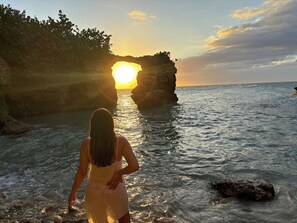 A person standing at the edge of a rocky shoreline with the sun setting behind a cliff. - Lovely country home with private pool in the hills above the town Las Piedras.  (Las Piedras)