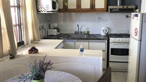 Une cuisine compacte équipée d’un four à micro-ondes, d’une cuisinière et d’un évier. On y trouve une table à manger recouverte d’une nappe à motifs et agrémentée d’une plante en pot.