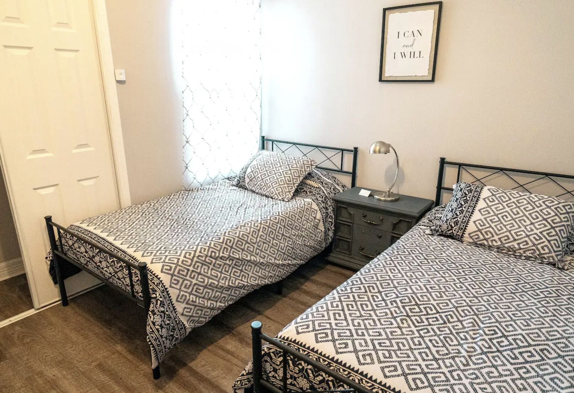A bedroom with two beds, each with patterned bedding, a bedside table with a lamp, and a framed inspirational quote on the wall.
