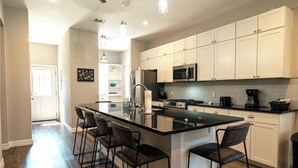 Una cocina moderna con una isla central, armarios blancos, electrodomésticos de acero inoxidable y taburetes de bar.