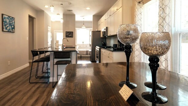 Una cocina con electrodomésticos modernos, un comedor con mesa de madera y dos objetos de vidrio decorativos en la encimera.