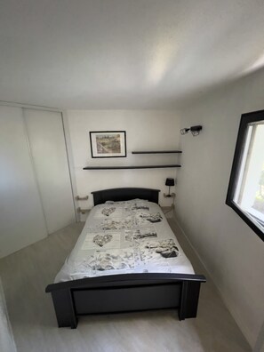 A bedroom with a bed, a framed picture on the wall, and a window.