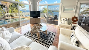 A spacious living room with a large TV, comfortable seating, and a view of the ocean through large windows. - Villa Morning Glory - Private Pool - Amazing Views (St Thomas)