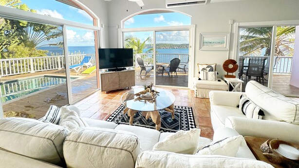 A spacious living room with a large TV, comfortable seating, and a view of the ocean. - Villa Morning Glory - Private Pool - Amazing Views (St Thomas)