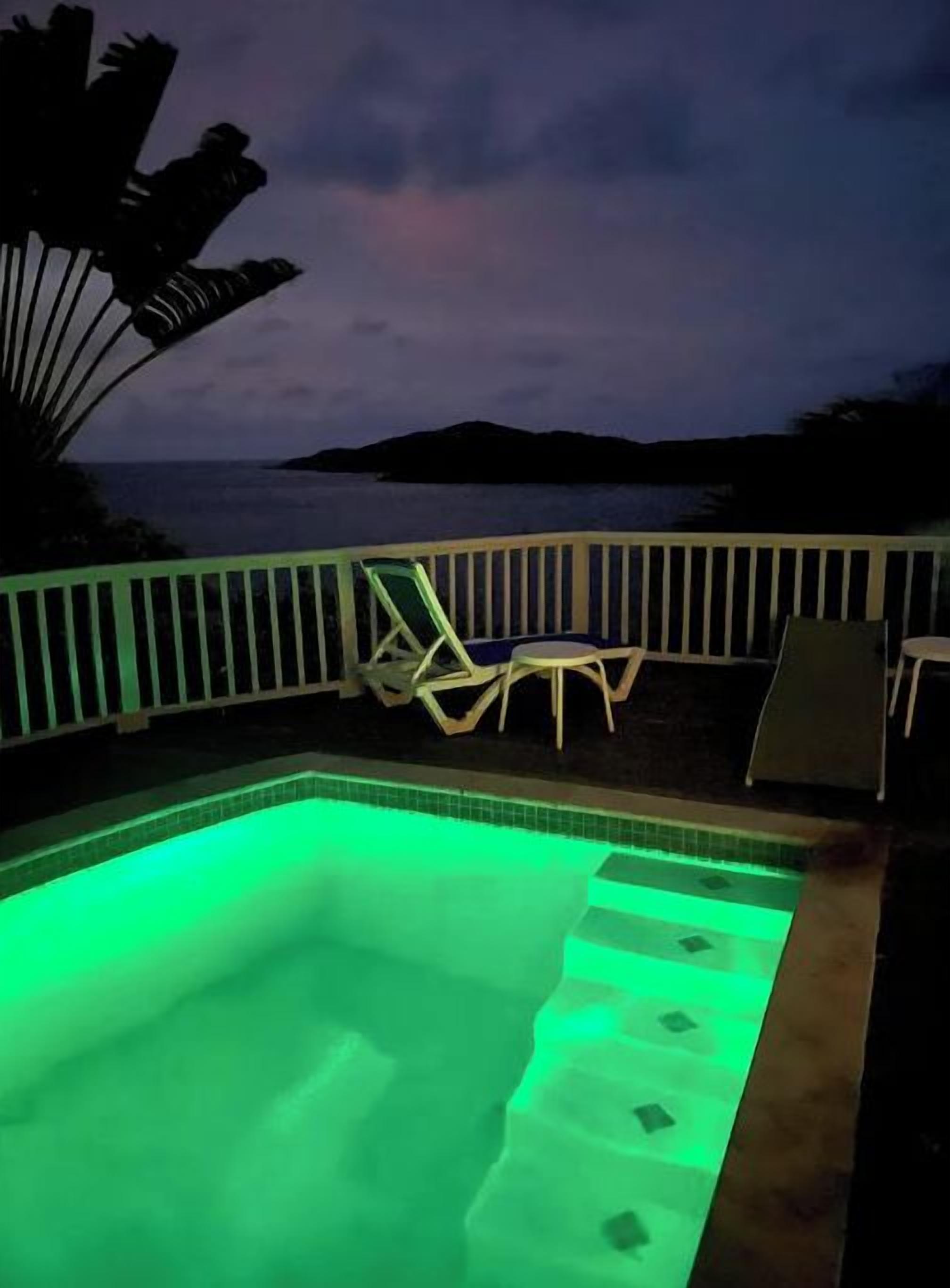 Ein Schwimmbecken mit grünem Licht, einem weißen Zaun und einem Stuhl.