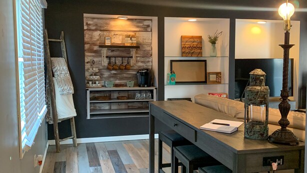 Una cocina moderna con salpicadero de madera, un comedor con mesa oscura y un ventilador de techo.
