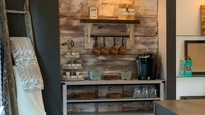 Una cocina con pared de madera rústica, una estación de café y una escalera apoyada en la pared.