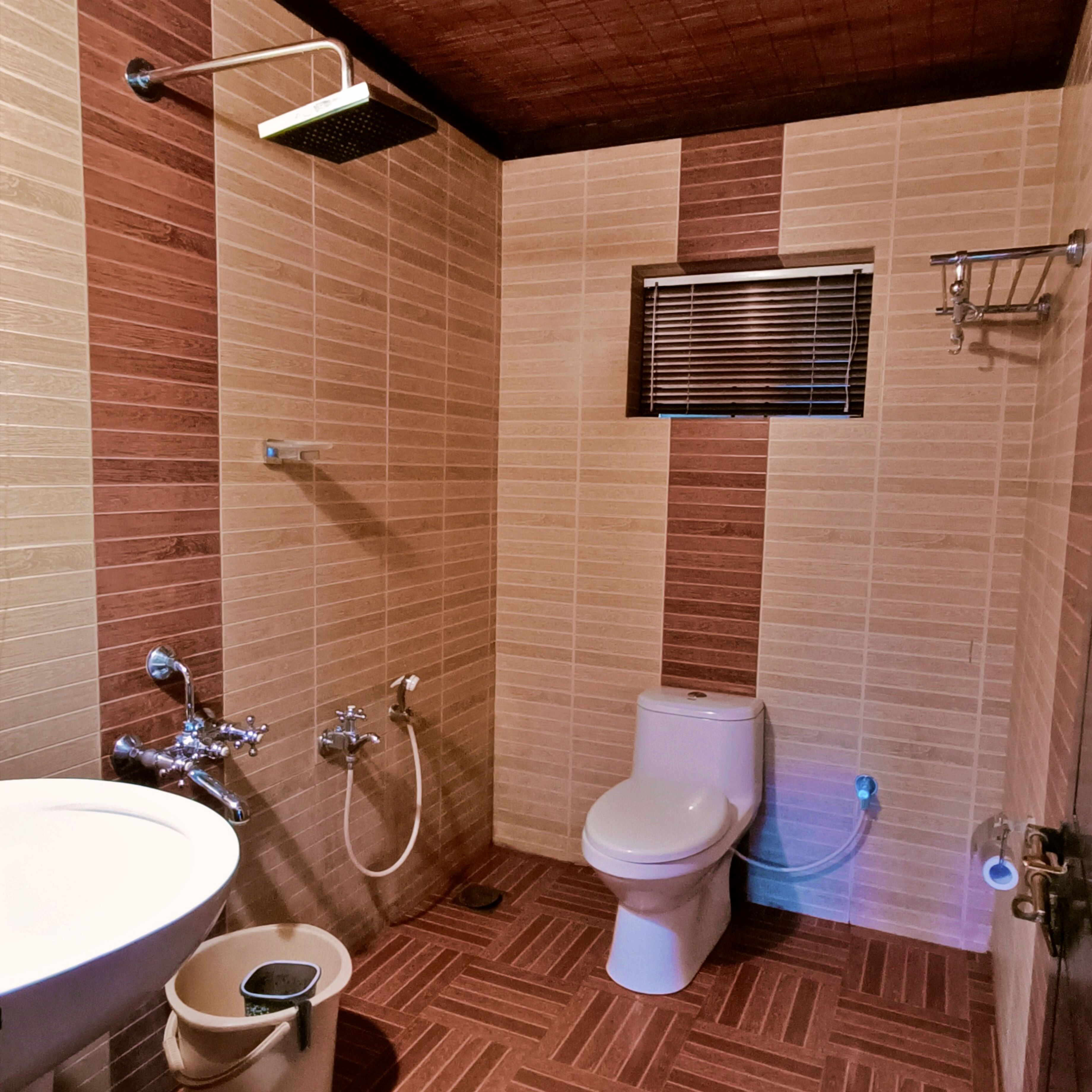 Ein Badezimmer mit Waschbecken, Toilette, Dusche und einem Fenster mit Jalousien.