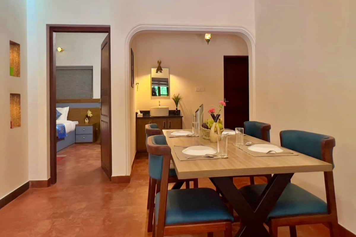 A dining area with a wooden table set for four, blue upholstered chairs, and a kitchen in the background.