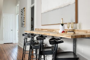 Une cuisine avec un plan de travail en bois, des tabourets de bar noirs, une bouteille de vin et deux verres.