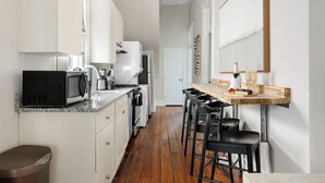 Une cuisine avec des meubles blancs, un plan de travail en bois et un coin bar avec des tabourets.