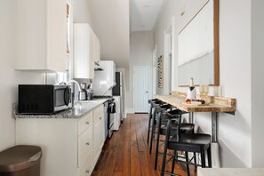 Cocina con armarios blancos, encimera de madera y barra con taburetes.