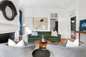 Ein Wohnzimmer mit einem grünen Sofa, zwei grauen Sesseln, einem Holztisch und einem Kamin.