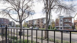 Una calle residencial con casas de varios pisos, cielo despejado y una valla metálica en primer plano.