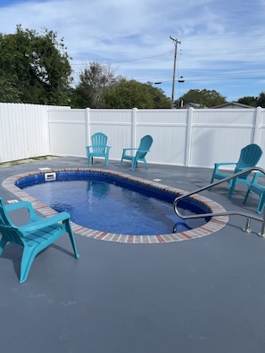 Ein Garten mit Swimmingpool, umgeben von einem weißen Zaun, mit mehreren türkisfarbenen Stühlen.