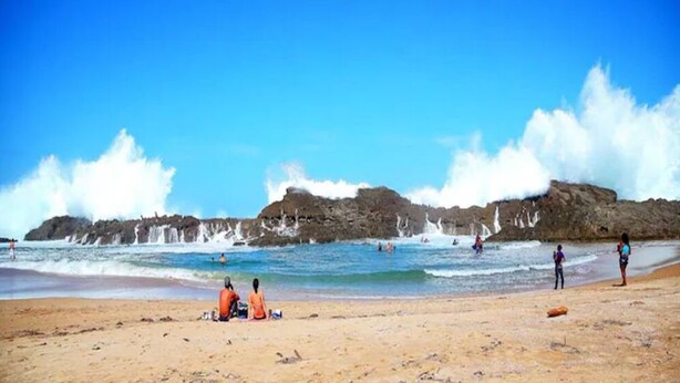 A beach with rocky cliffs, clear blue sky, and people enjoying the water.