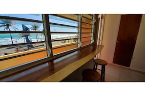 A room with a large window overlooking a beach, a wooden bench, and a door.