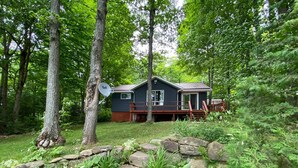 A cabin with a deck, surrounded by a stone wall and lush greenery. - Dawson Loop Inn - Private Lakefront Cottage (MONT)